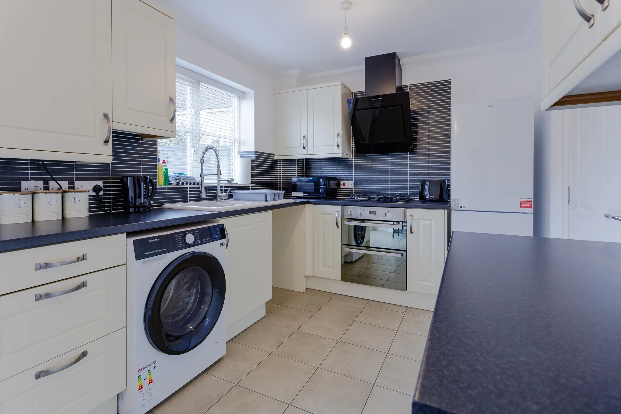 Modern kitchen with cream cabinets, dark blue tiles, and integrated appliances