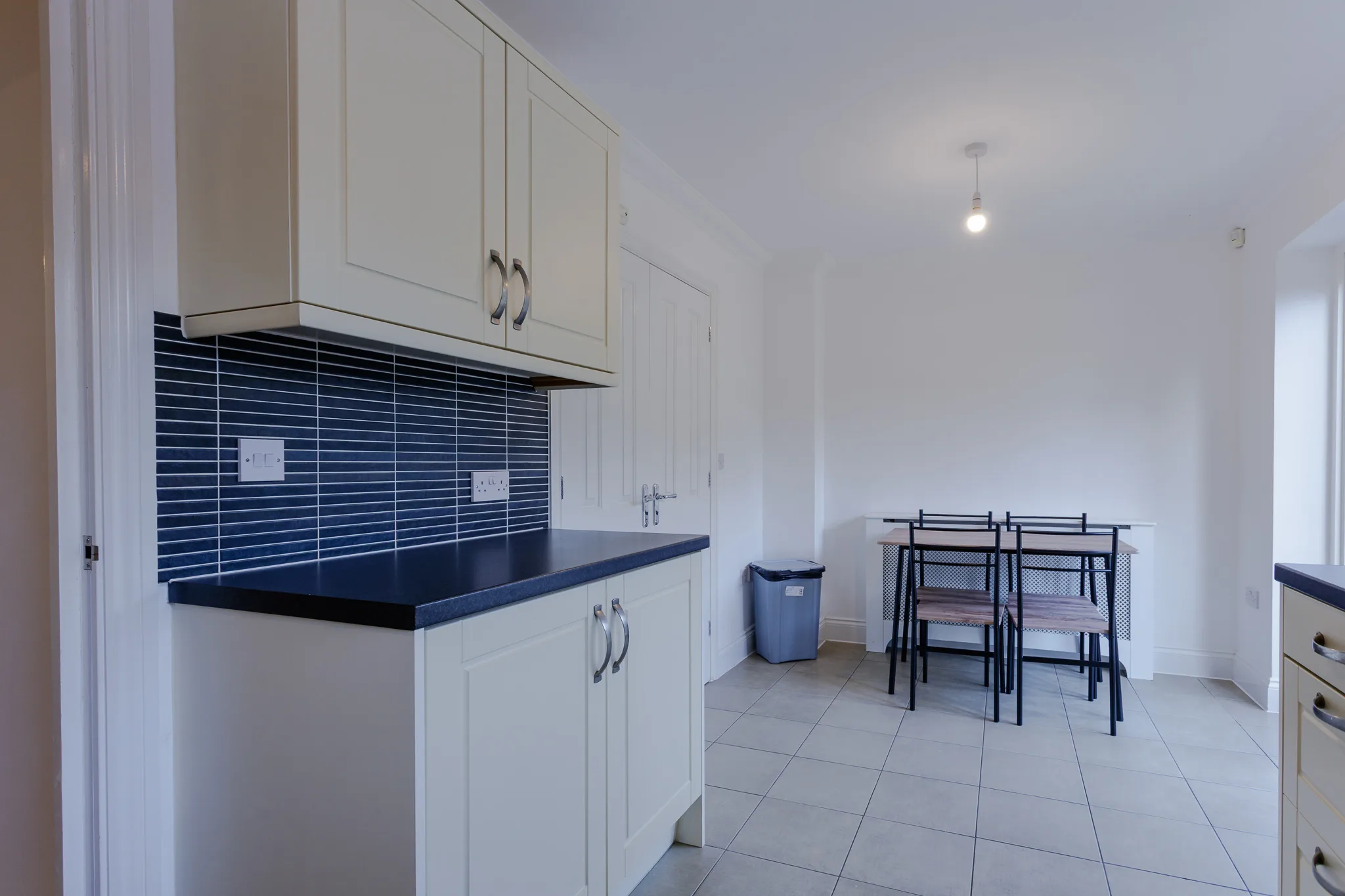 Modern kitchen with white cabinets, navy tiles and dining area