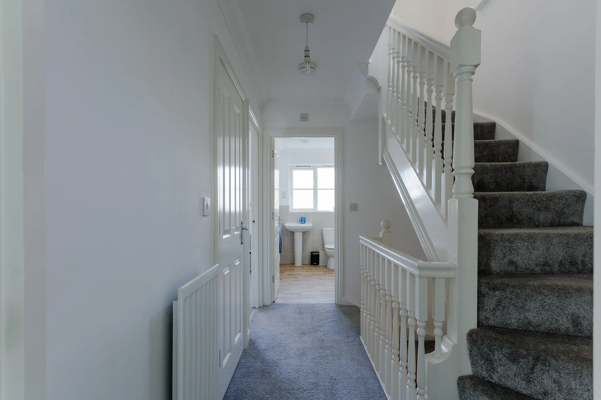 Modern white hallway with staircase and bathroom entrance