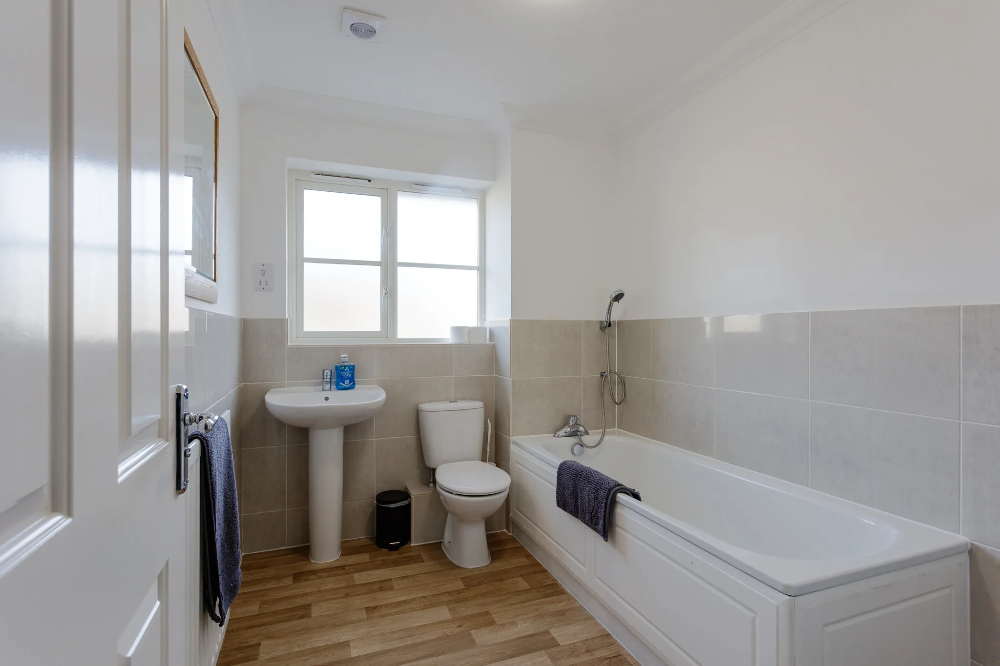 Modern bathroom with white walls, beige tiles, and wooden flooring