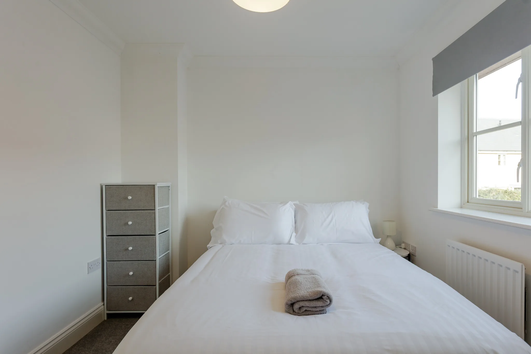 Minimalist bedroom with white bed and grey storage drawer
