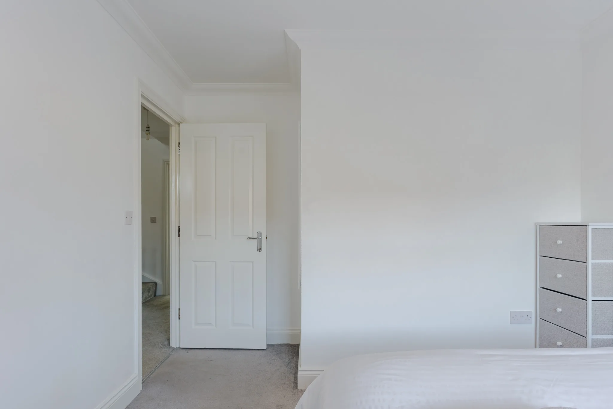 Minimalist bedroom with white door and grey storage unit