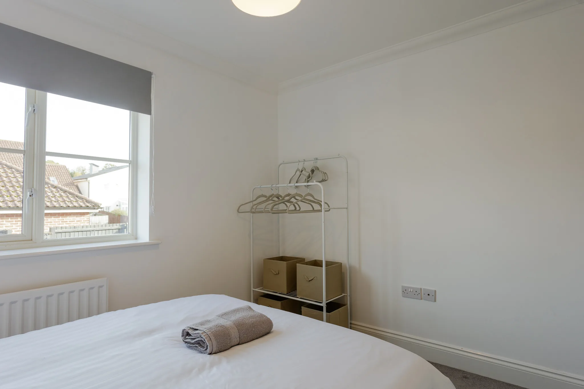 Minimalist bedroom with white bed, clothing rail, and window