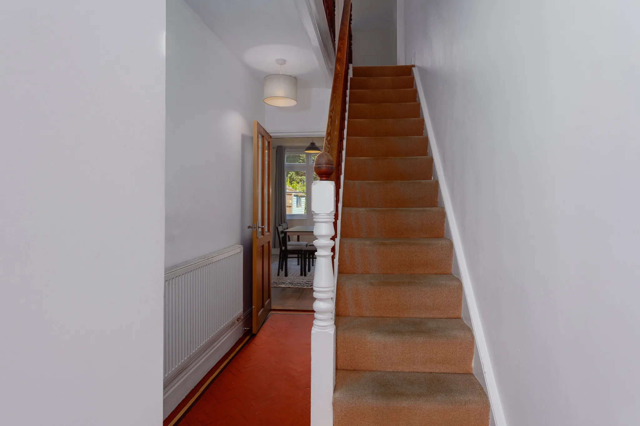 Bright hallway with wooden staircase and red carpet runner