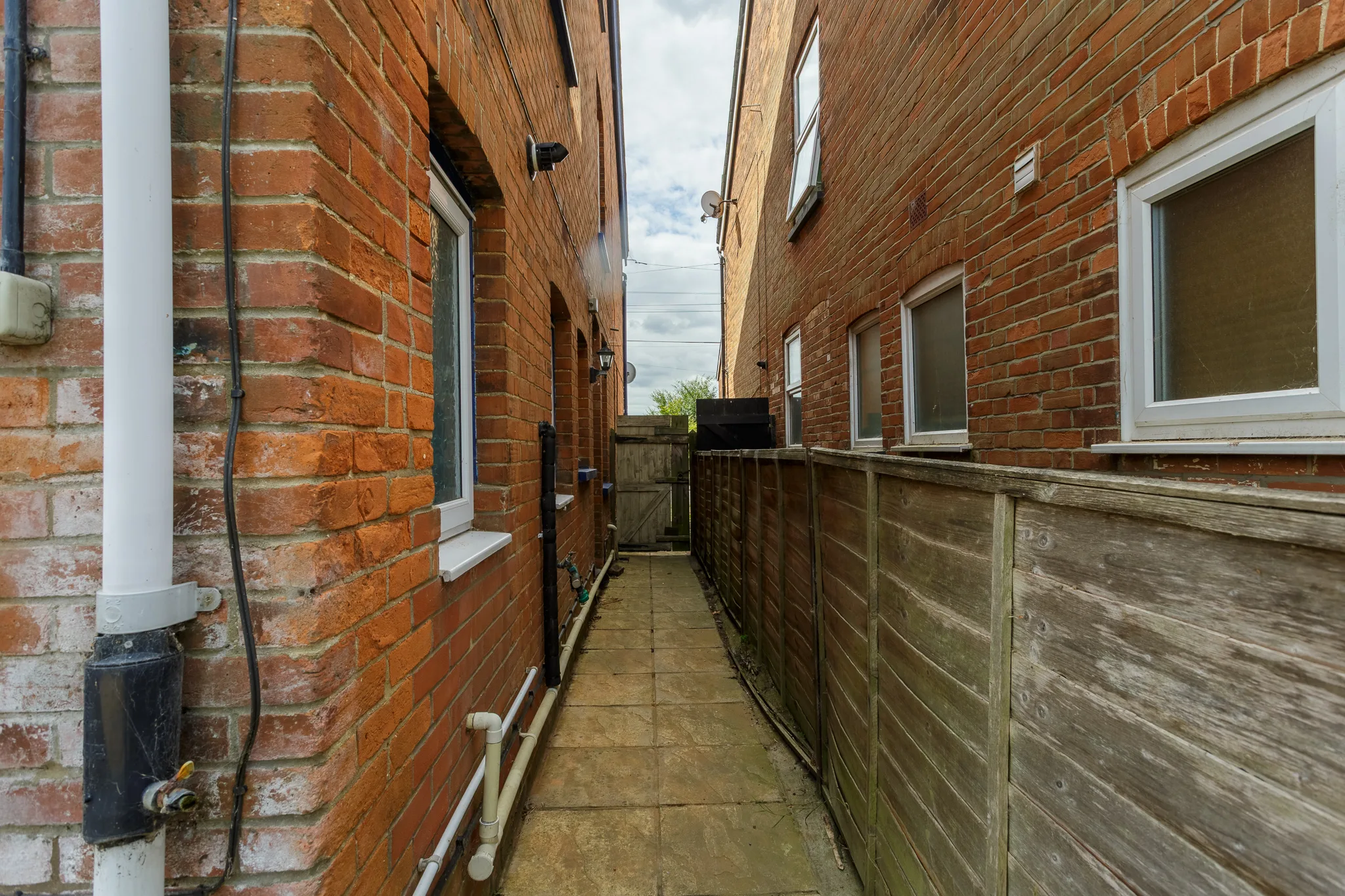 Narrow alleyway between red brick buildings with wooden fencing