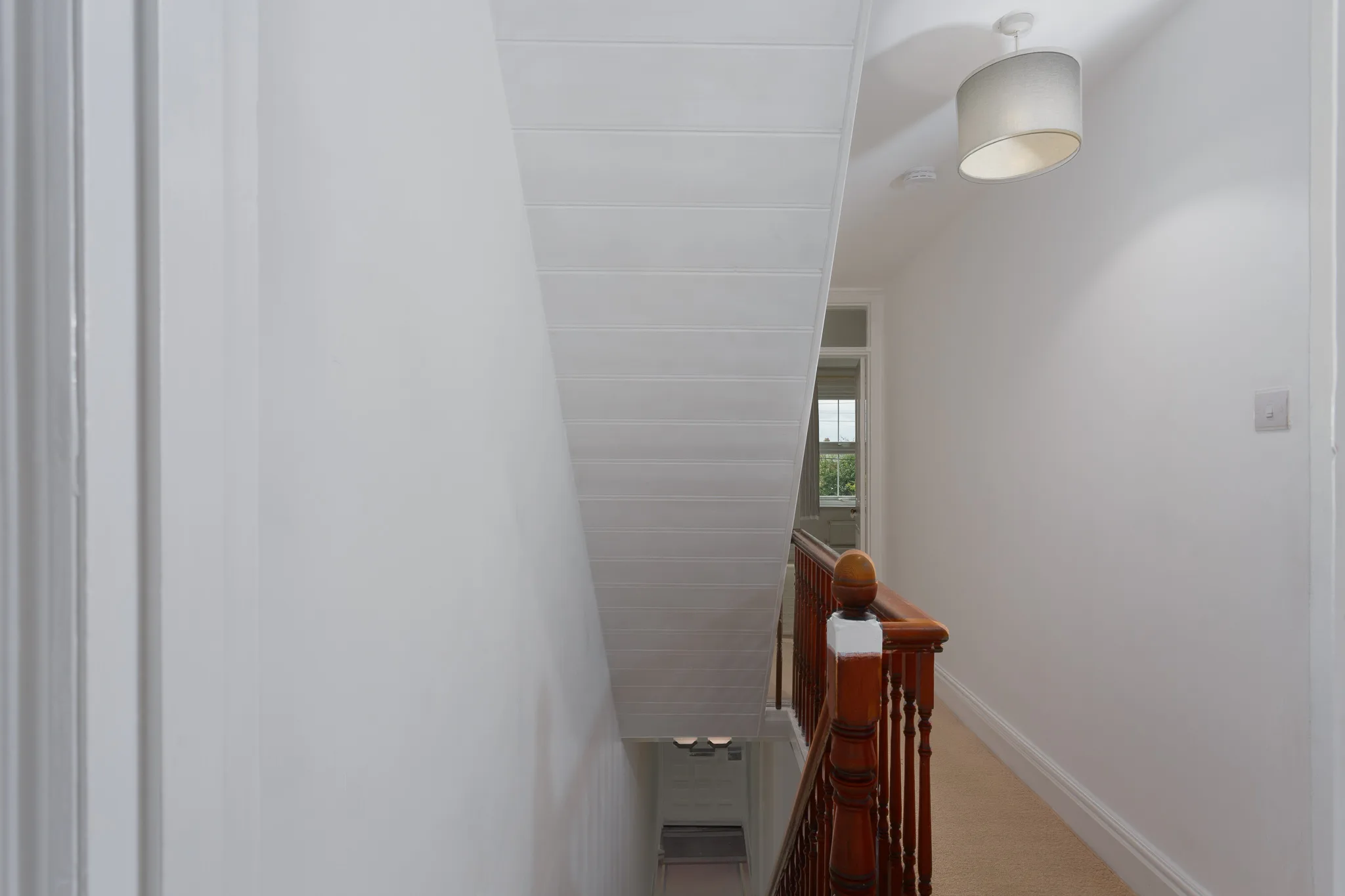 Modern hallway with wooden staircase railing and pendant light