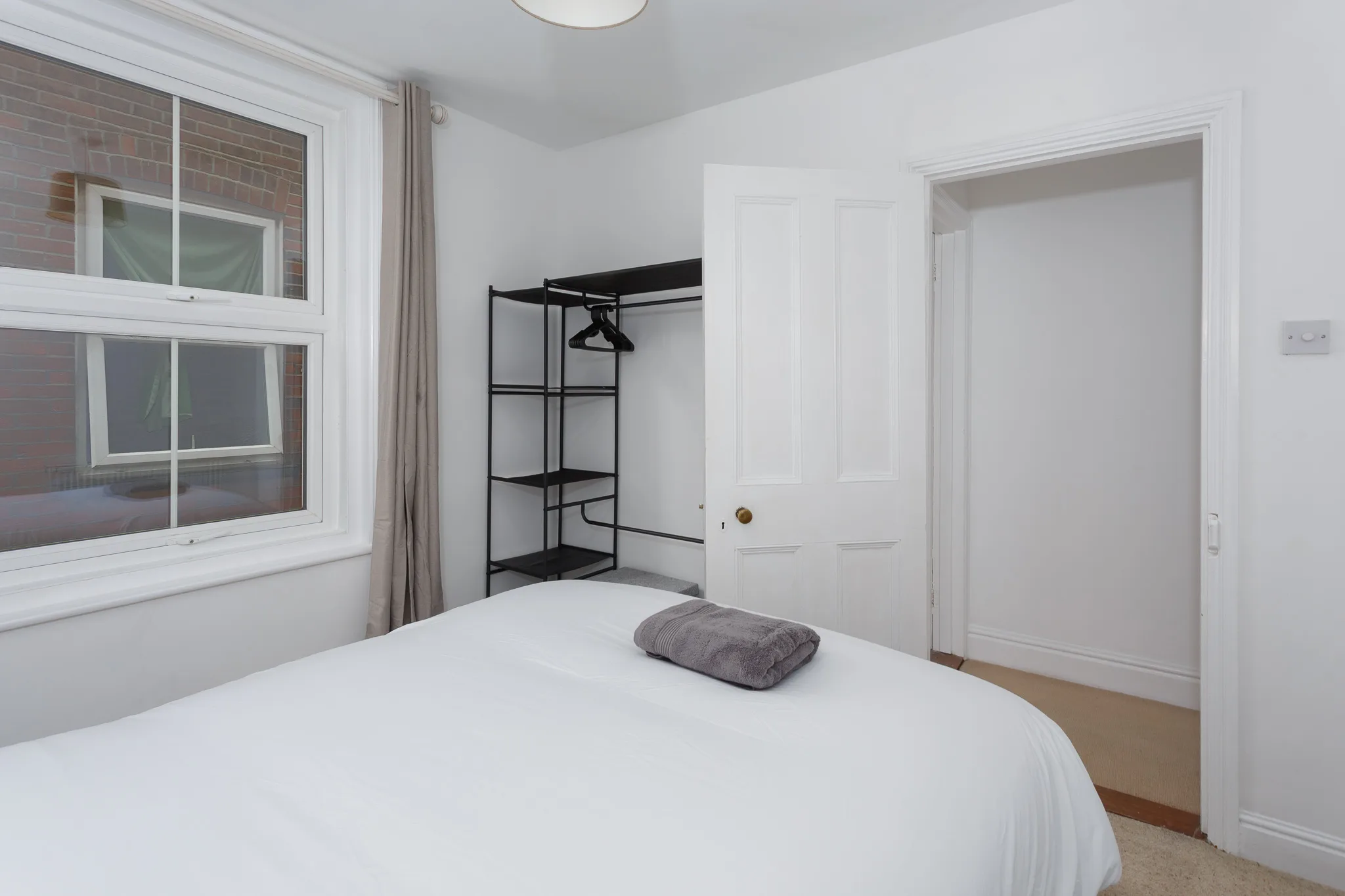 Modern minimalist bedroom with white bed and black metal shelving unit