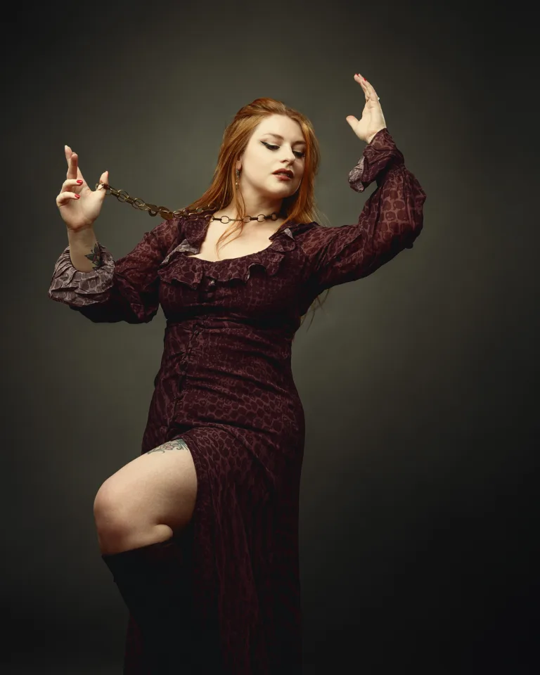 Woman in burgundy velvet dress holding decorative chain