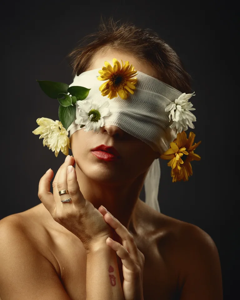 Woman with eyes covered by white bandage surrounded by flowers