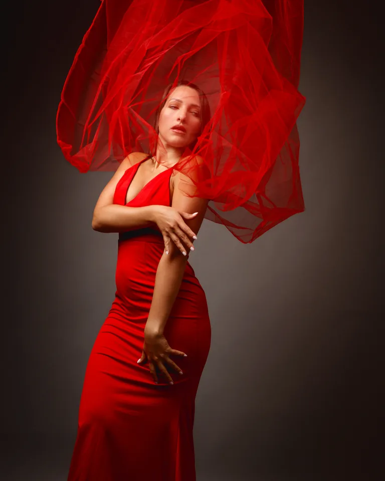 Woman in elegant red dress with flowing fabric backdrop