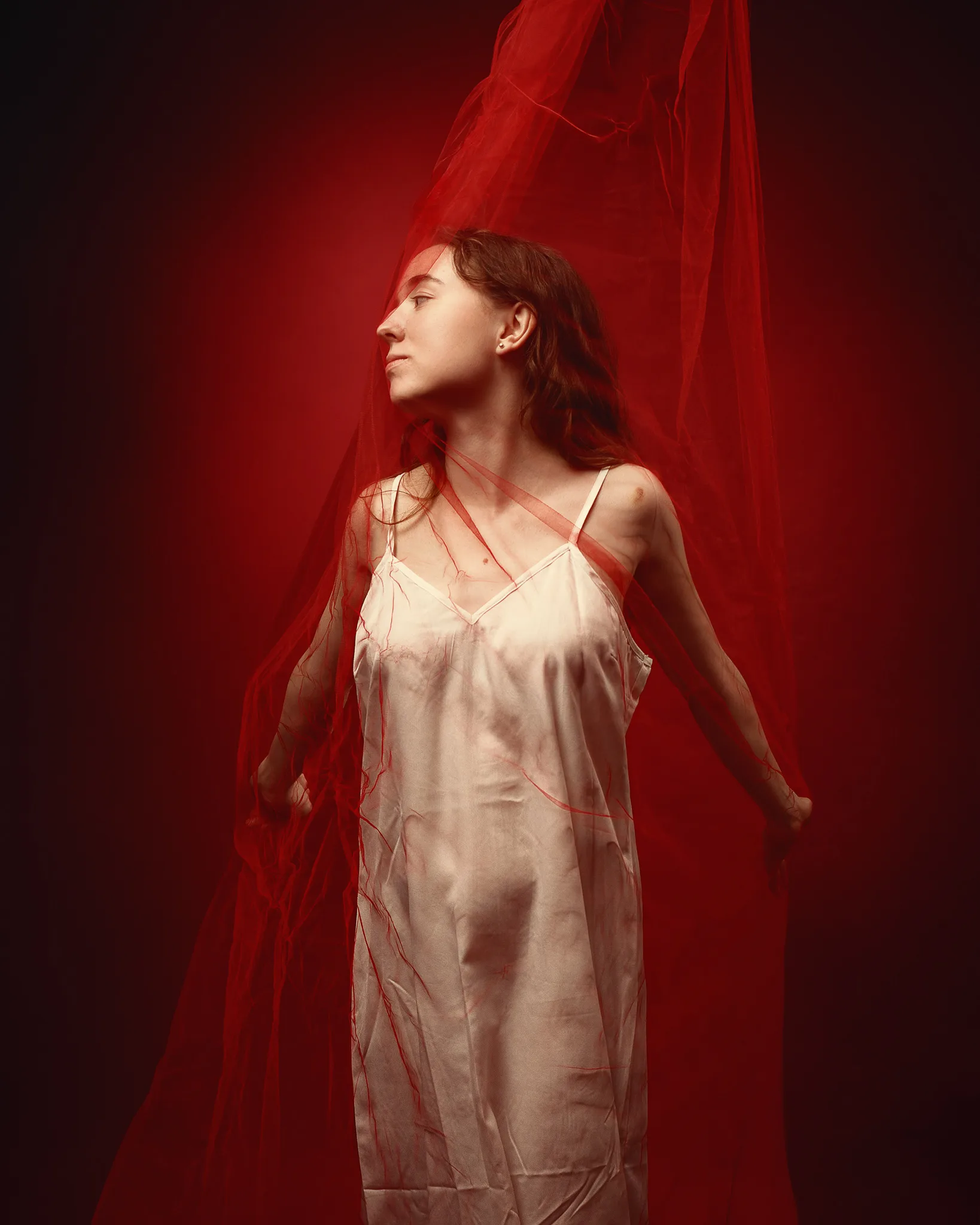 A woman in a pale slip dress stands in profile against a deep red background, draped in sheer red fabric.