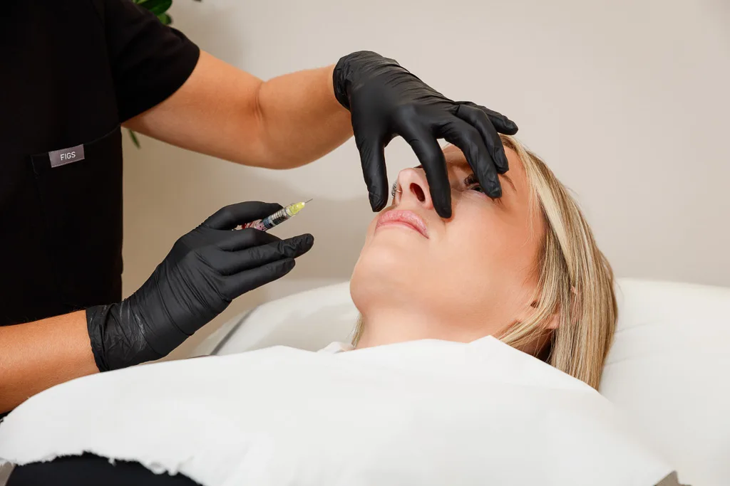 A healthcare professional in black gloves administers a facial injection to a patient lying down during a cosmetic procedure.