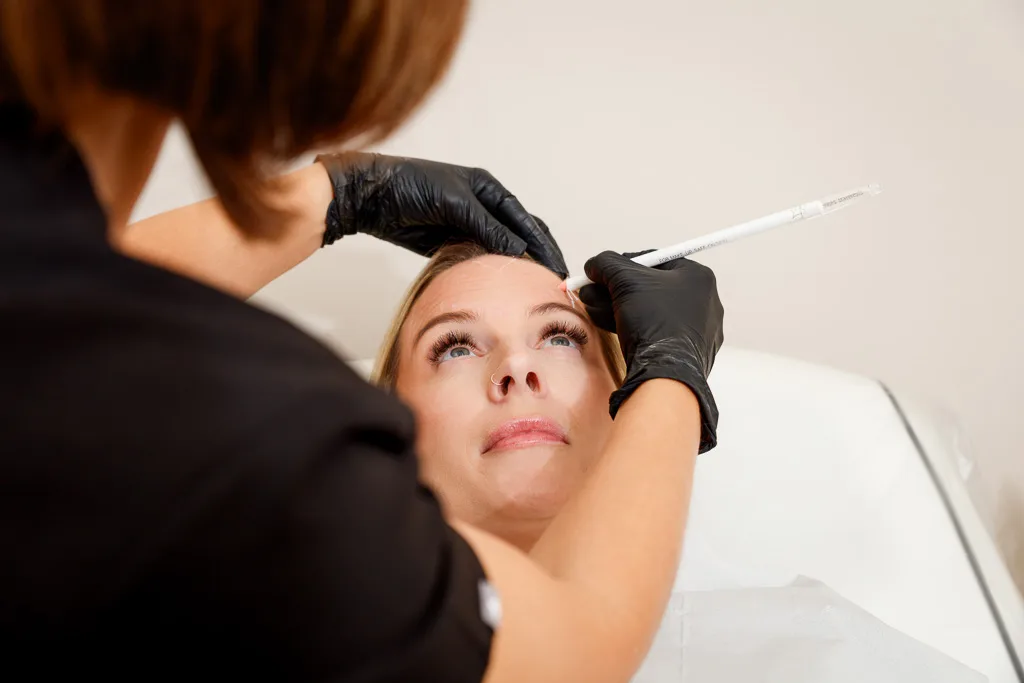 A practitioner in black gloves applies injectable treatment to a client's forehead during a cosmetic procedure.
