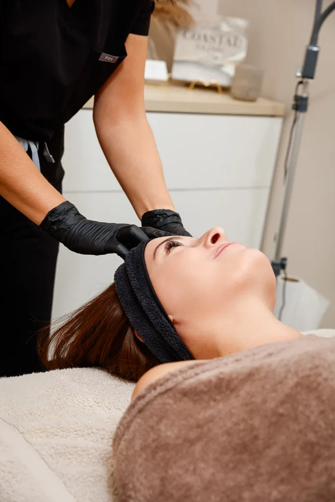 A person receiving a facial treatment from a practitioner wearing black gloves in a clinical beauty setting.